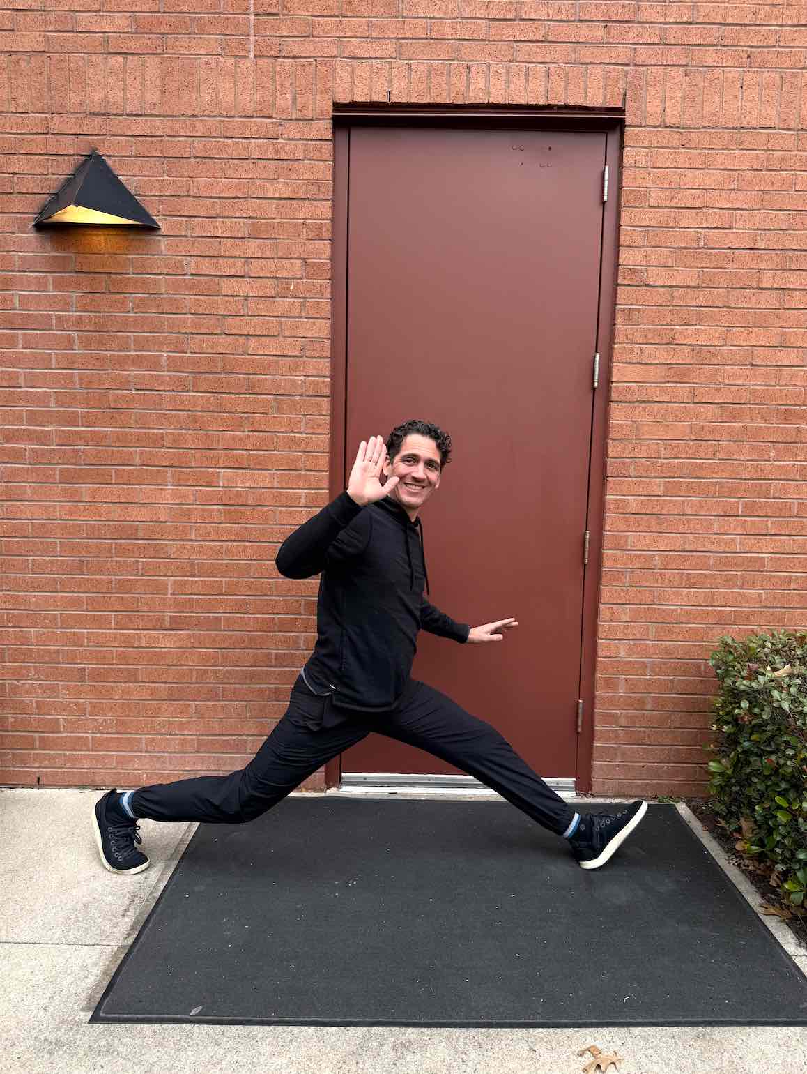 Gregg stretching his legs in a wide stance outside the door of a brick building