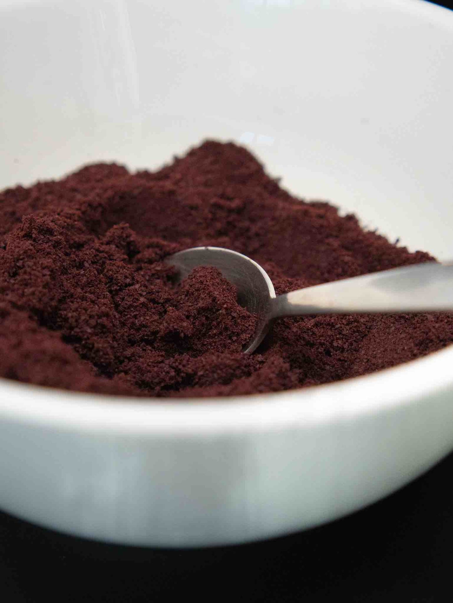 Close-up of dark purple acai powder in a white bowl with a spoon