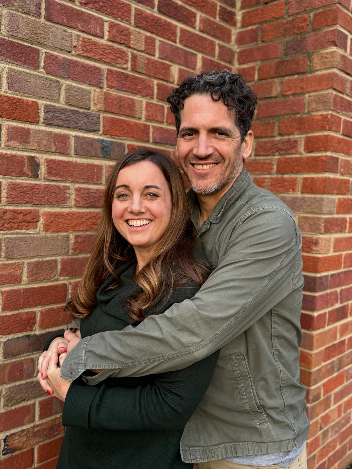 Man and woman hugging in front of a brick wall
