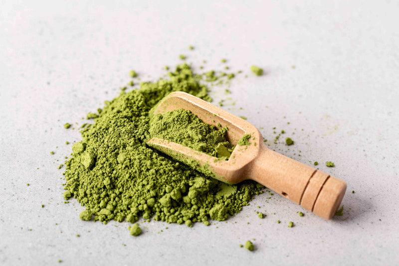 Wooden scoop filled with green matcha powder on a light gray surface