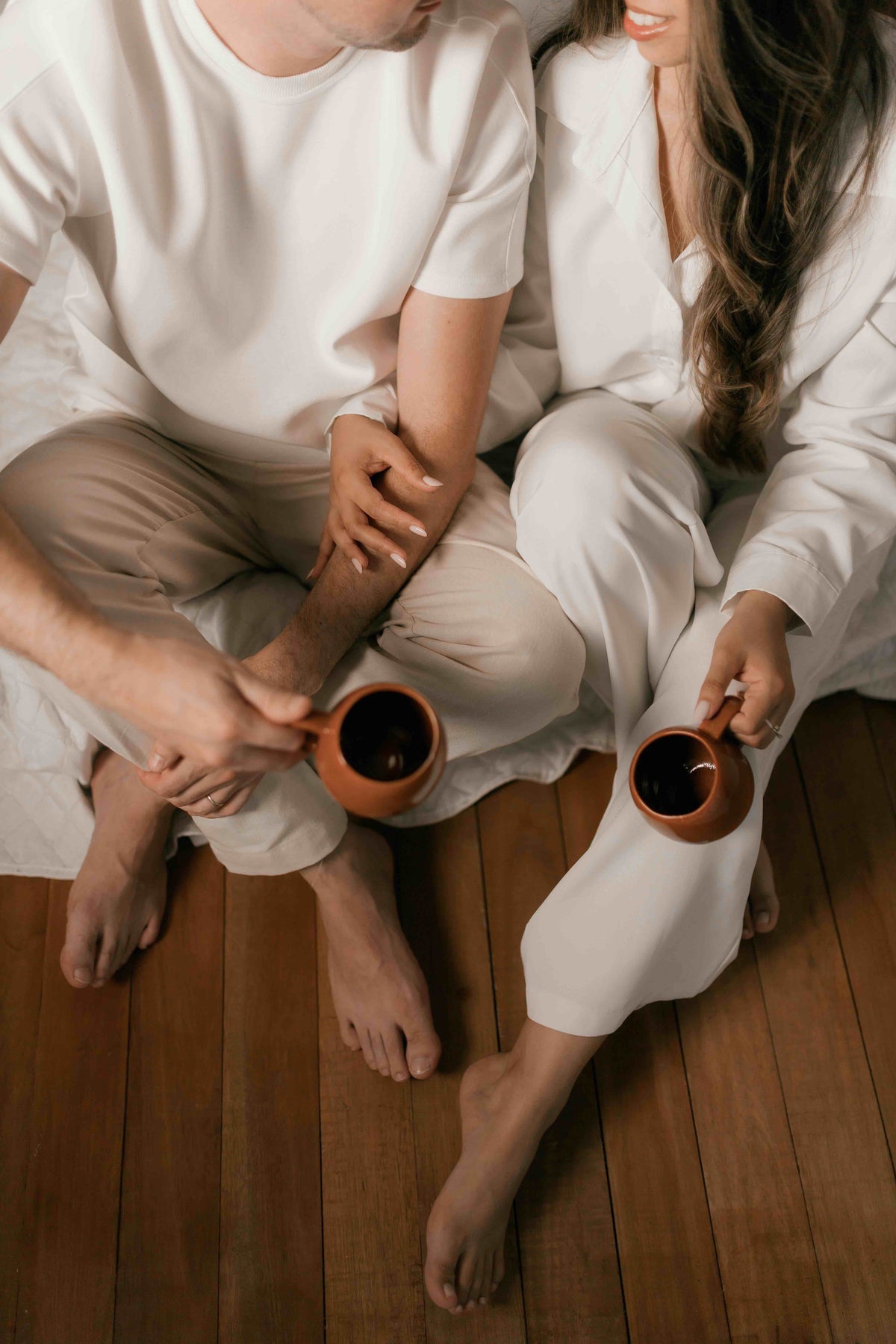 Two people sitting on a wooden floor holding small cups.